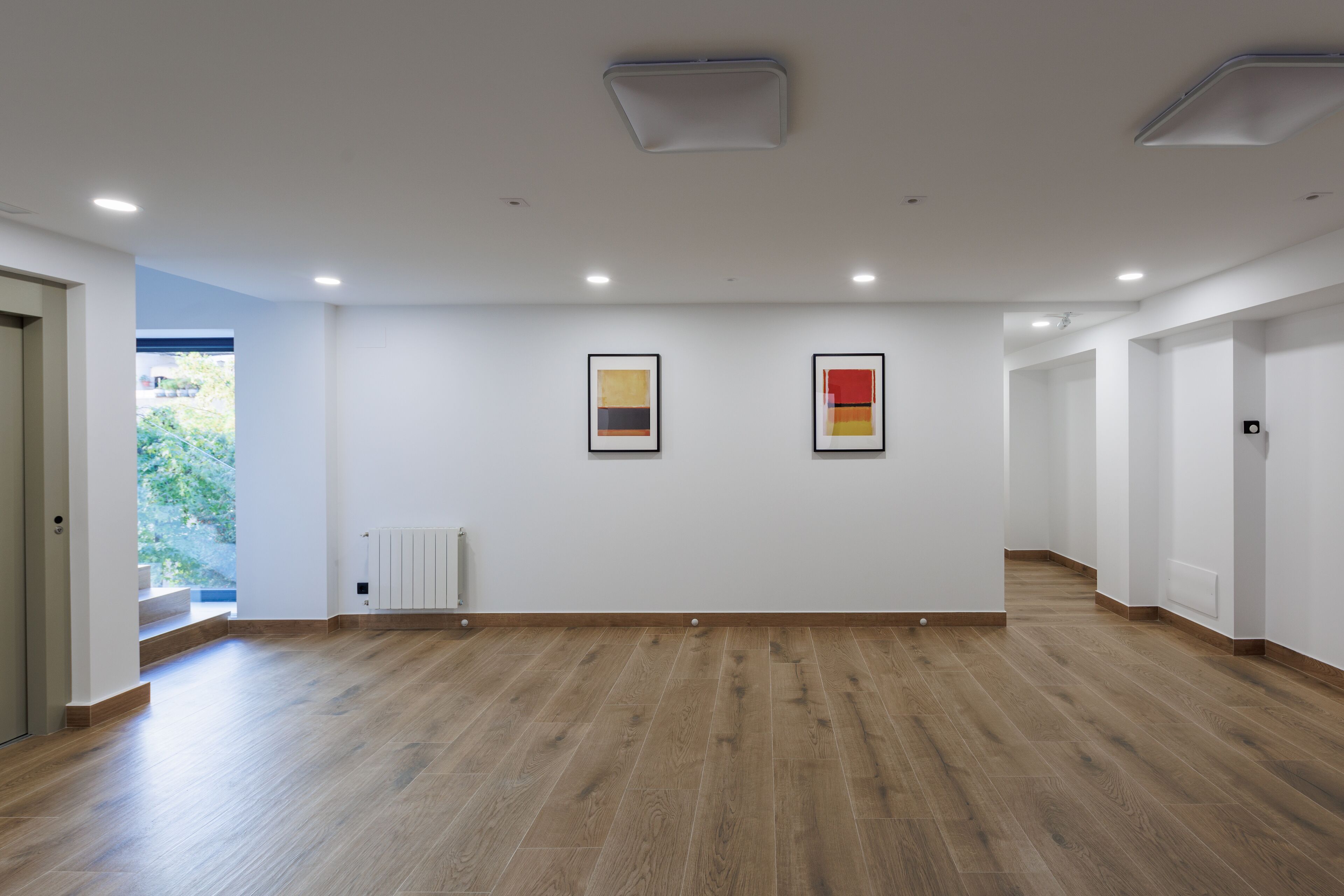A spacious, modern hotel room with a wooden floor, white walls, and minimalistic decor.
