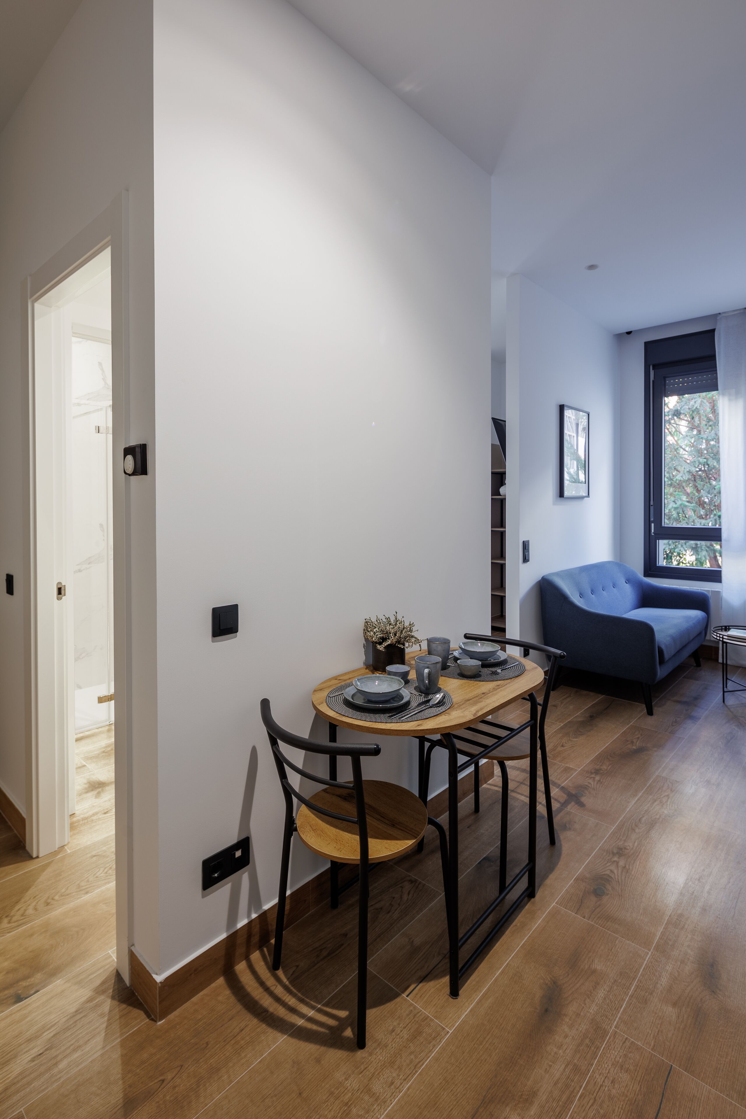 A modern living space with a dining area, a sofa, and a window.