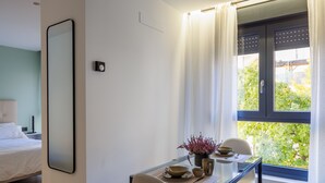 A modern hotel room with a dining area featuring a glass table, white chairs, and a view of greenery outside. - APARTAMENTOS CONGRESO PARKING GRATUITO (Logroño)