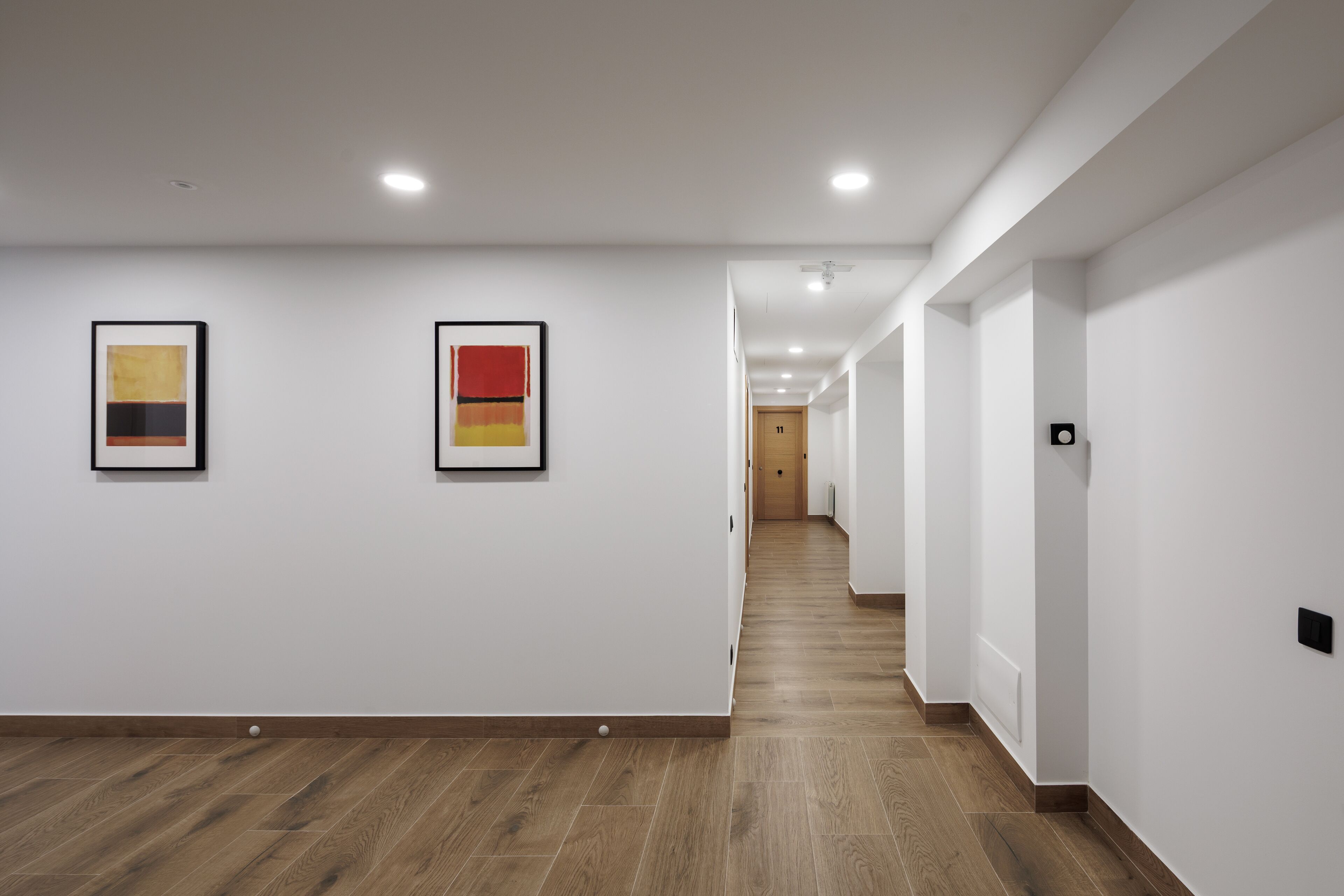 A hallway with wooden flooring, white walls, and two framed artworks.