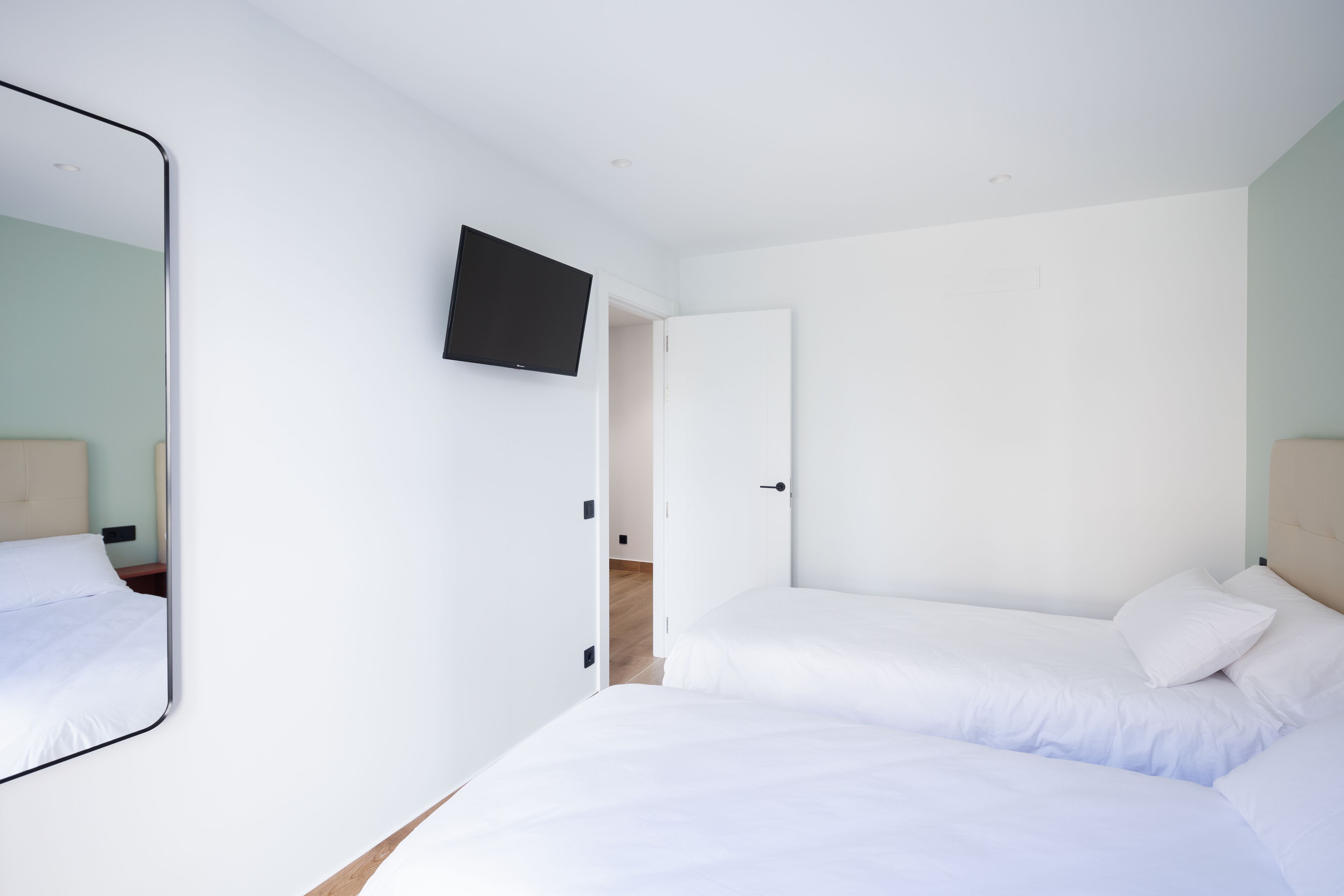 A bedroom with a single bed, a TV mounted on the wall, and a door leading to another room.