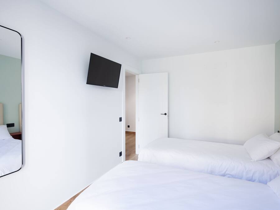 A bedroom with a single bed, a TV mounted on the wall, and a door leading to another room.