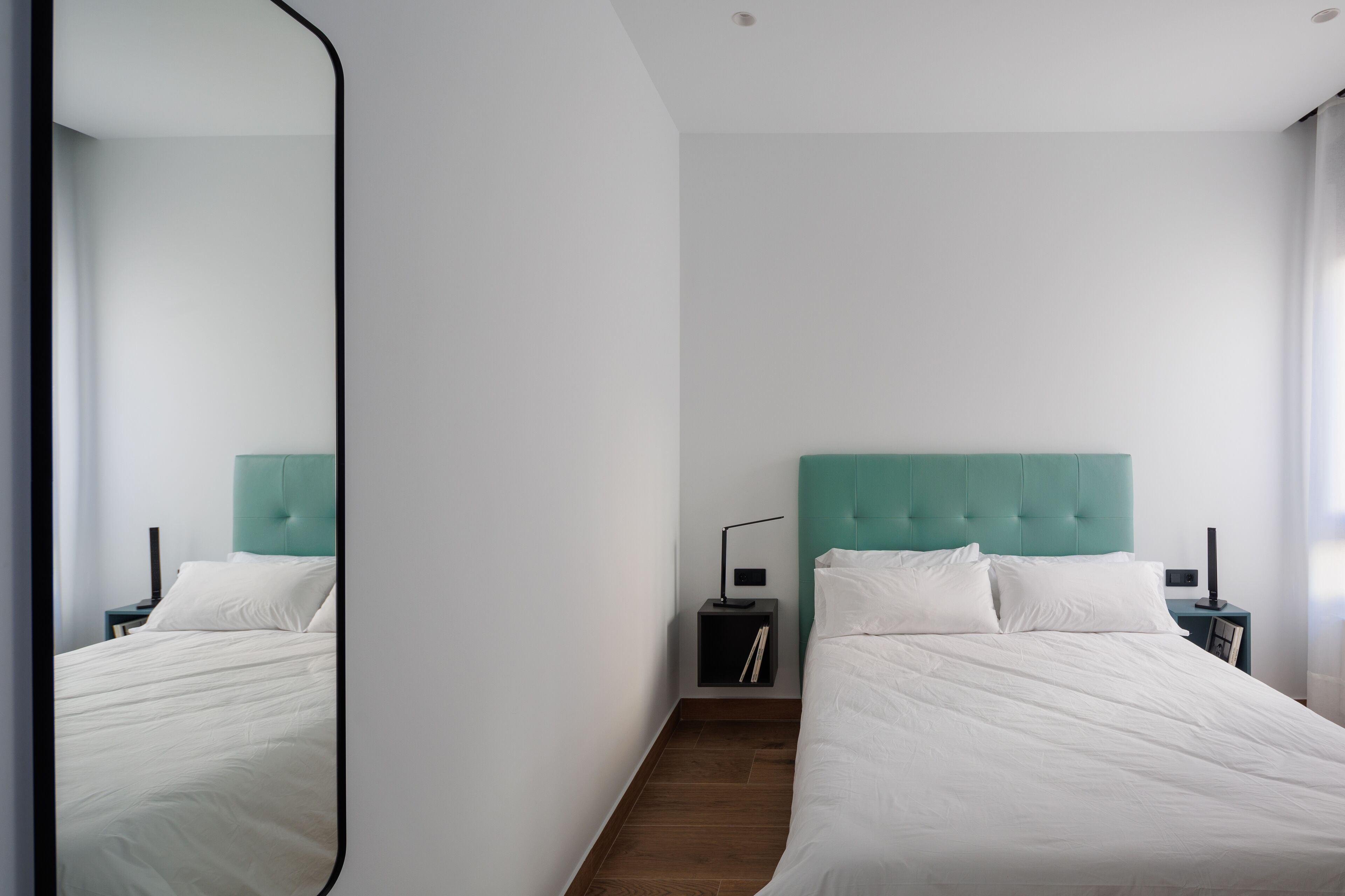 Une chambre moderne avec deux lits, une tête de lit de couleur turquoise, du linge de lit blanc et une table de chevet avec une lampe.