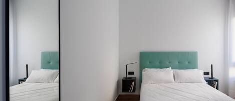 Une chambre moderne avec deux lits, une tête de lit de couleur turquoise, du linge de lit blanc et une table de chevet avec une lampe.