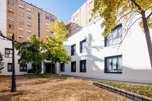 A courtyard with a white building, a tree, and a paved area.