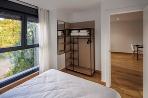 A bedroom with a large window, a bed, a wardrobe, and a desk with a chair.