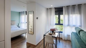 A modern room with a bed, a dining table with chairs, a sofa, and a large window with curtains. - APARTAMENTOS CONGRESO PARKING GRATUITO (Logroño)