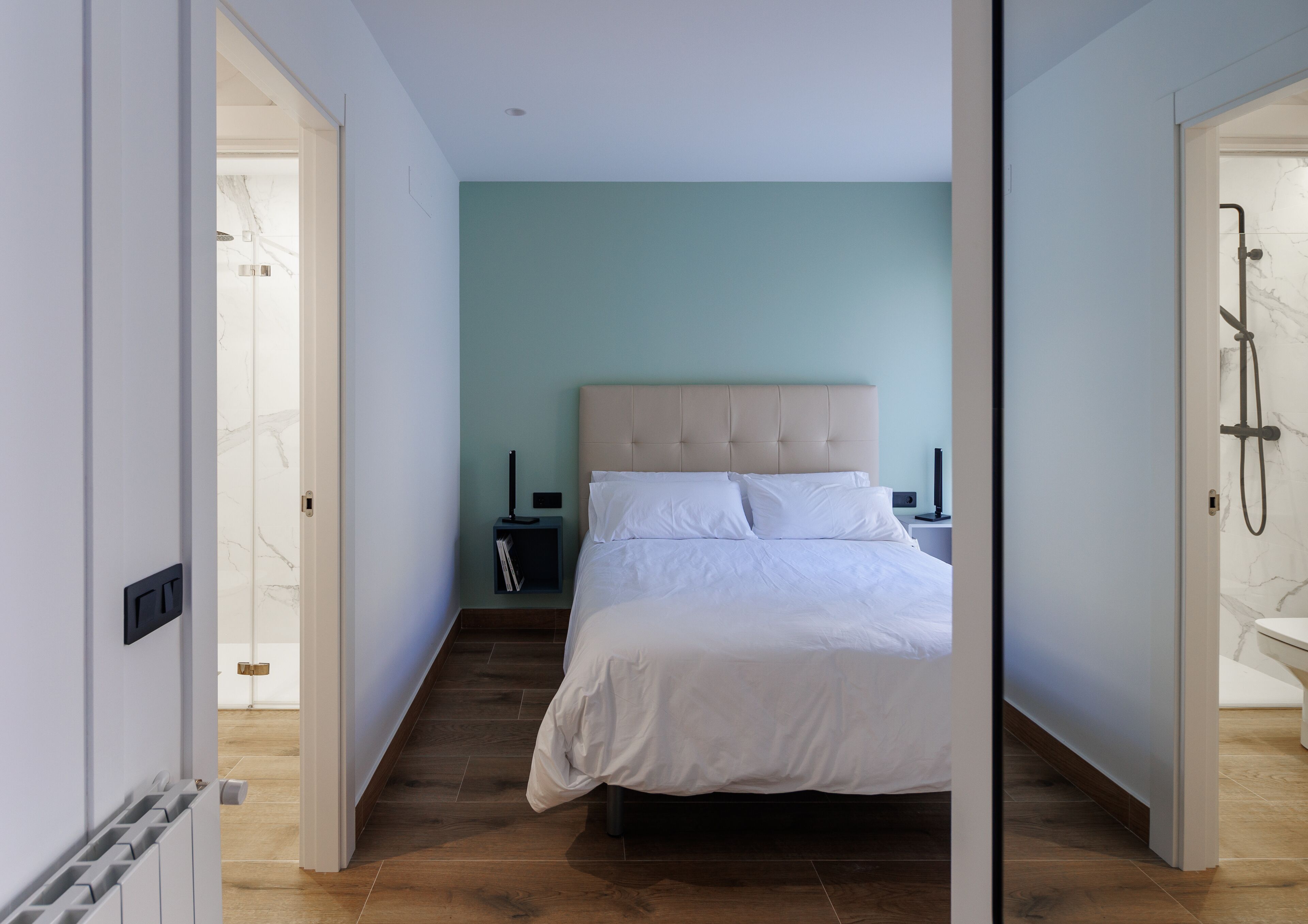 Un dormitorio con cama, mesitas de noche, una lámpara de pared y zona de ducha.