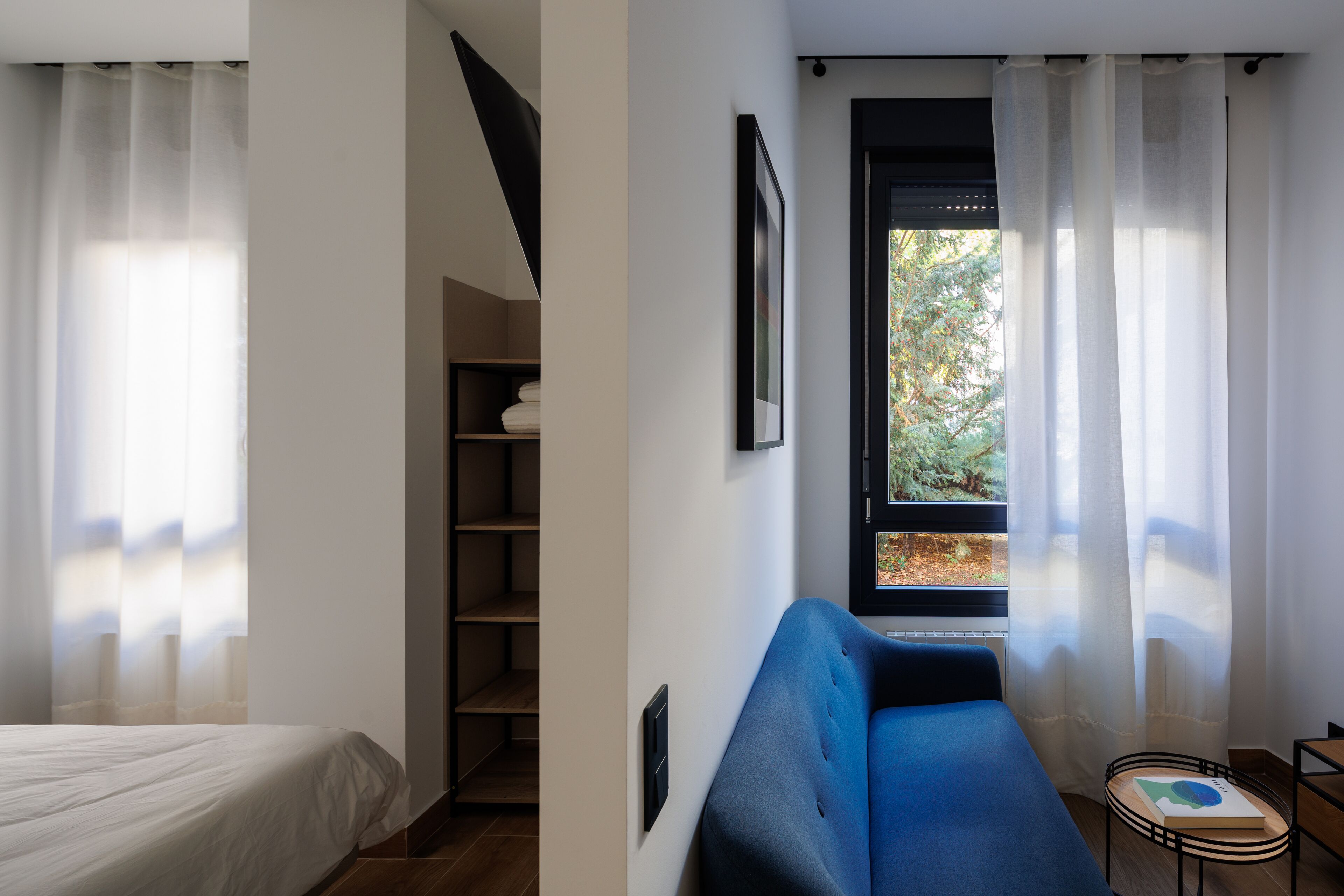 Una habitación con cama, un sofá azul, una mesita y una ventana con cortinas.