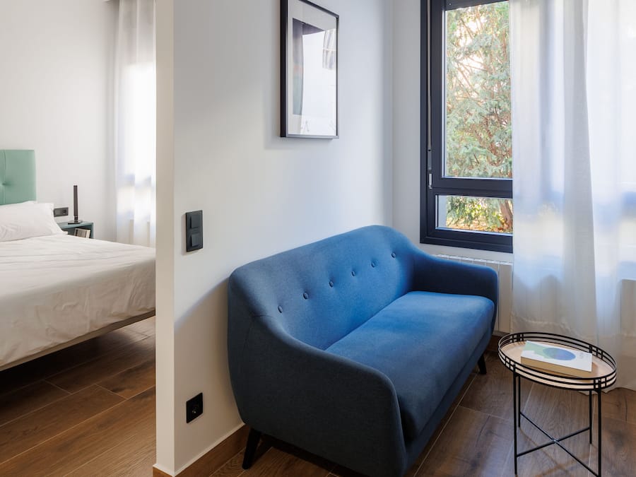 Quarto moderno com sofá azul, mesa redonda pequena e cama com cabeceira verde.