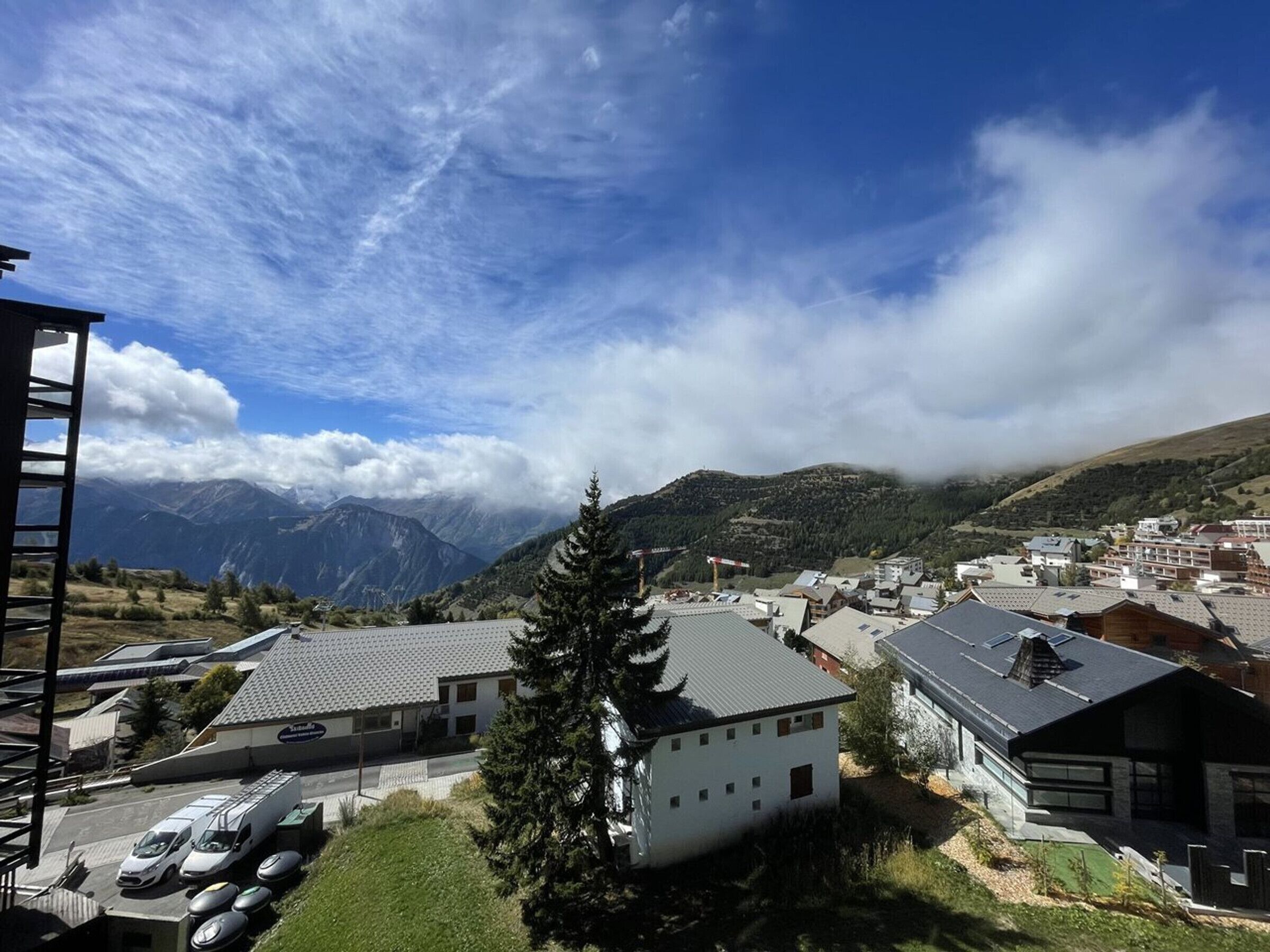 Un paysage montagneux avec une ville au premier plan, caractérisé par des bâtiments modernes à toits plats et un mélange de constructions résidentielles et commerciales.