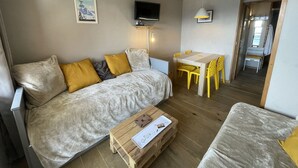 Un salon chaleureux avec un canapé, une table basse en bois et une table à manger entourée de chaises jaunes.