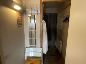 Um quarto pequeno com uma cama, um espelho, um cabideiro e uma placa indicando cerveja gratuita.
