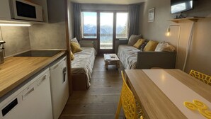 Une chambre d’hôtel compacte comprenant un coin cuisine, un canapé, une table à manger et un téléviseur fixé au mur.