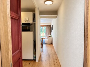 A hallway leading to a kitchen with a built-in oven and a dining area with a chair and table.