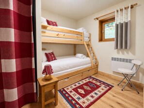 A compact room with a bunk bed, a small table, a chair, a radiator, and a window with curtains.