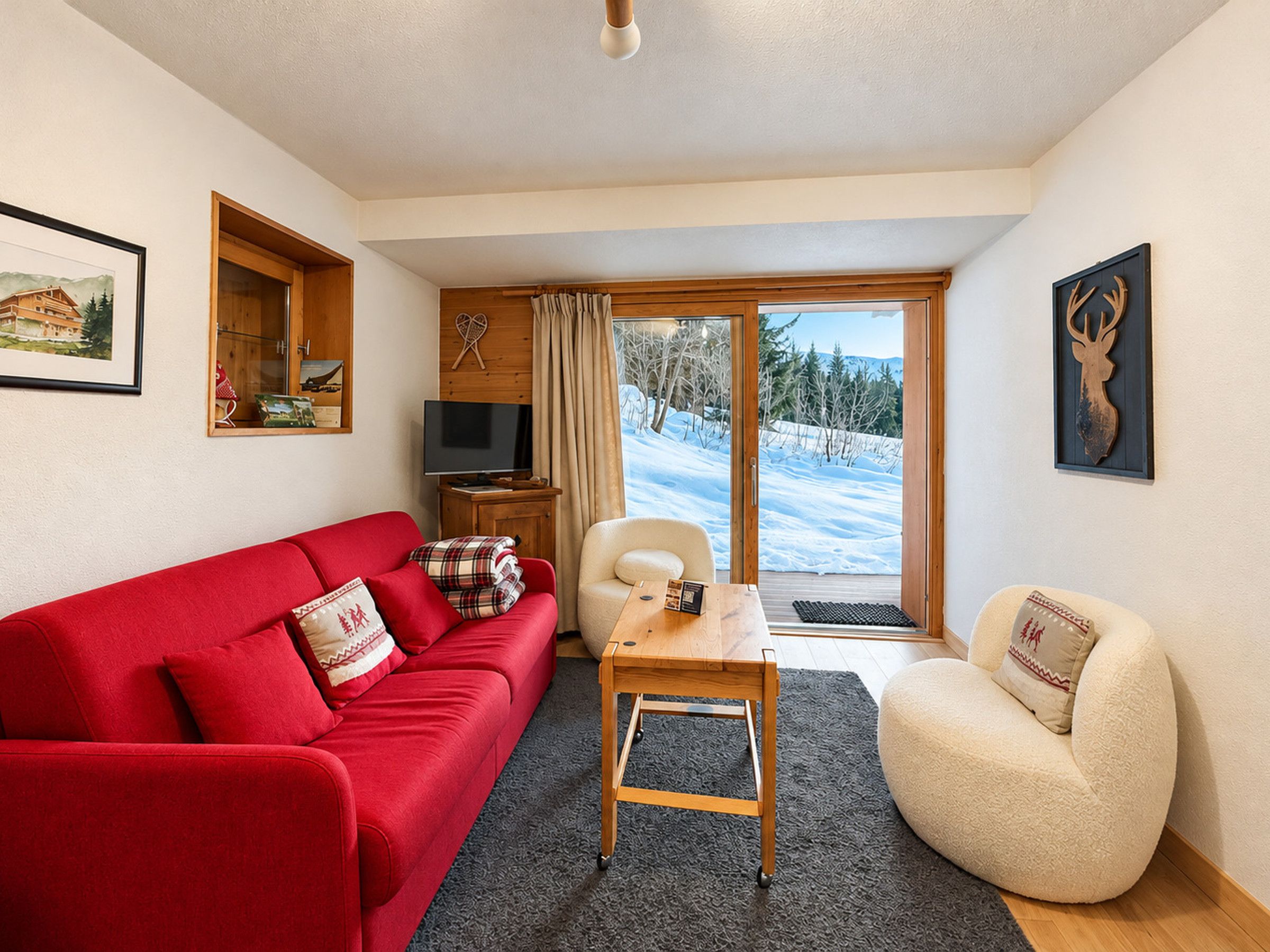 A cozy living room with a red sofa, a white armchair, a wooden coffee table, and a television on a wooden stand.