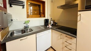 Eine kleine Küche mit Geschirrspüler, Spüle, Fenster mit Holzrahmen und einer Edelstahl-Dunstabzugshaube.