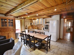 A rustic kitchen with wooden cabinets, a dining table with chairs, and a refrigerator. - Renovated chalet for 8 near center and slopes with parking (Morzine)
