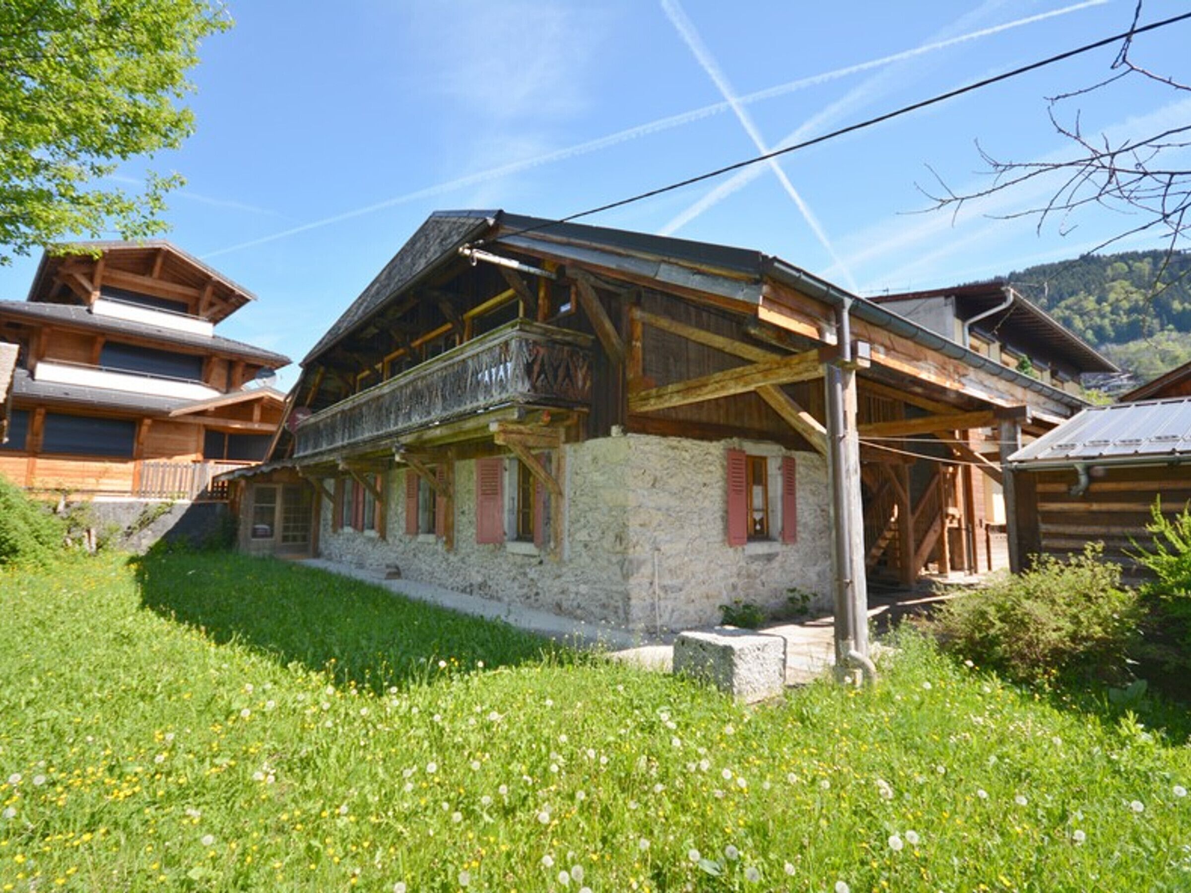 A traditional wooden chalet with a stone foundation, a balcony, and a stone staircase leading to the entrance.