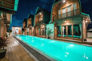 A poolside view of a resort with wooden villas, a swimming pool, and potted plants. - Andi Beach House (Canggu)