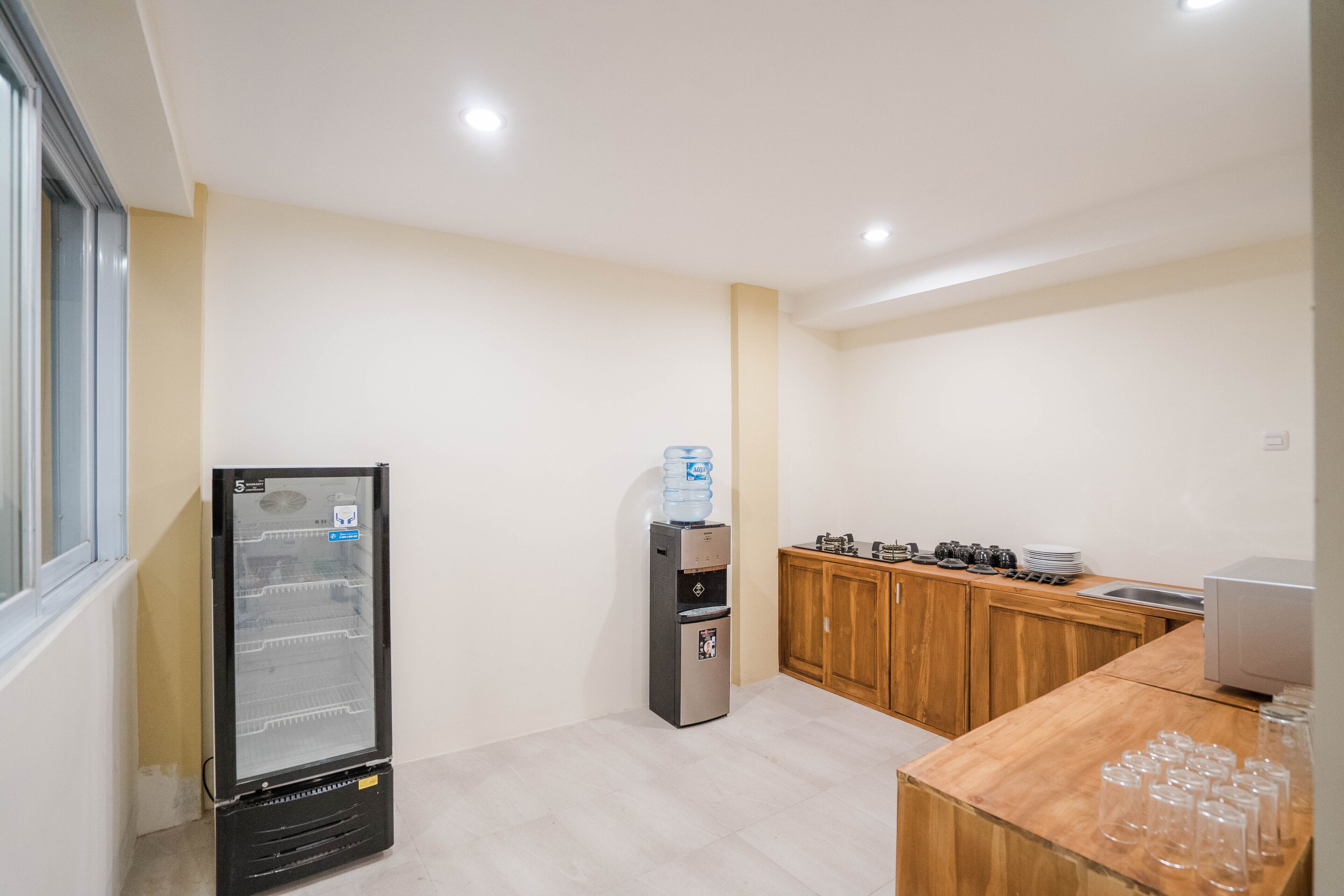 A compact kitchen with a refrigerator, water dispenser, wooden cabinets, and a countertop with glasses.