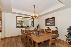 Un comedor con mesa de madera, sillas, una araña, un espejo y un cuadro enmarcado en la pared.