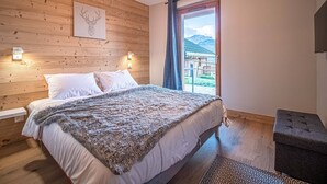 A bedroom with a wooden headboard, a bed with white linens, a fluffy blanket, a bedside table, and a view of a wooden structure outside. - 3* Chalet Valmorel, ski-in/ski-out, 3 bedrooms, parking, WIFI (Valmorel)