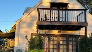 A two-story building with a balcony and a front door. - Firefly Resort: House & Cottage on 10 acres. BBQ deck, pool, tennis court, lawns (Firefly)