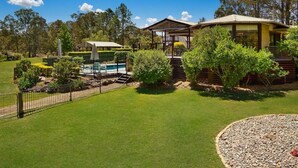 A two-story house with a swimming pool, surrounded by a well-maintained lawn and a fence. - Firefly Resort: House & Cottage on 10 acres. BBQ deck, pool, tennis court, lawns (Firefly)