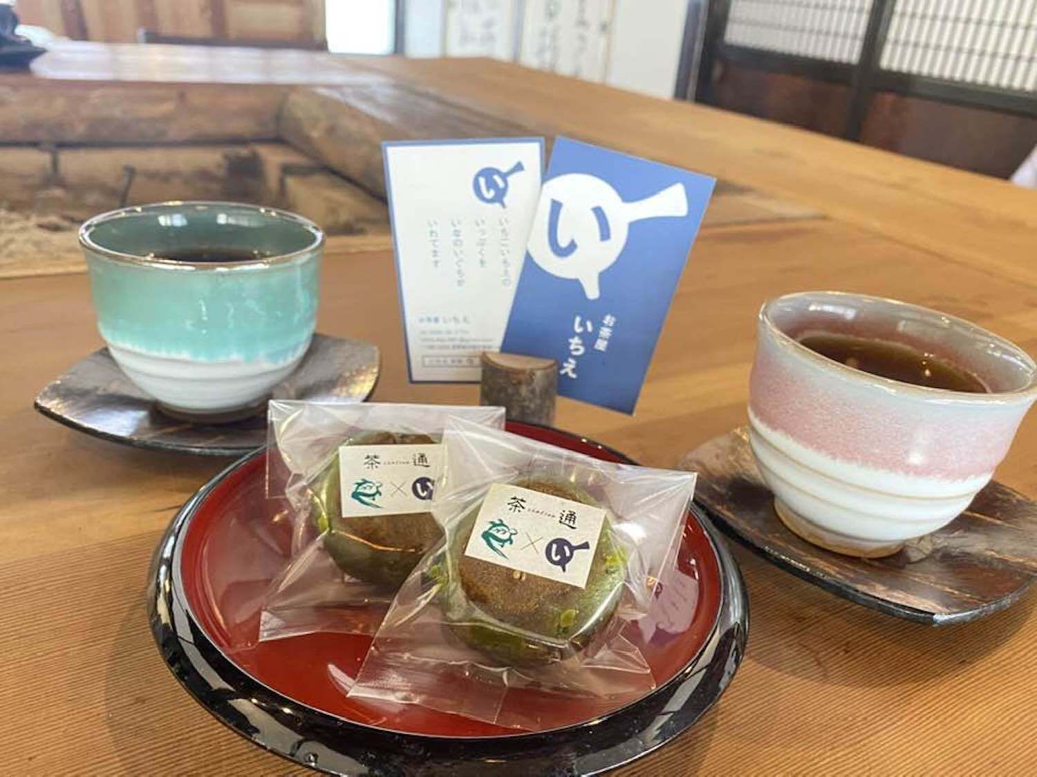 A table with two packaged snacks, two cups of tea, and a dessert.