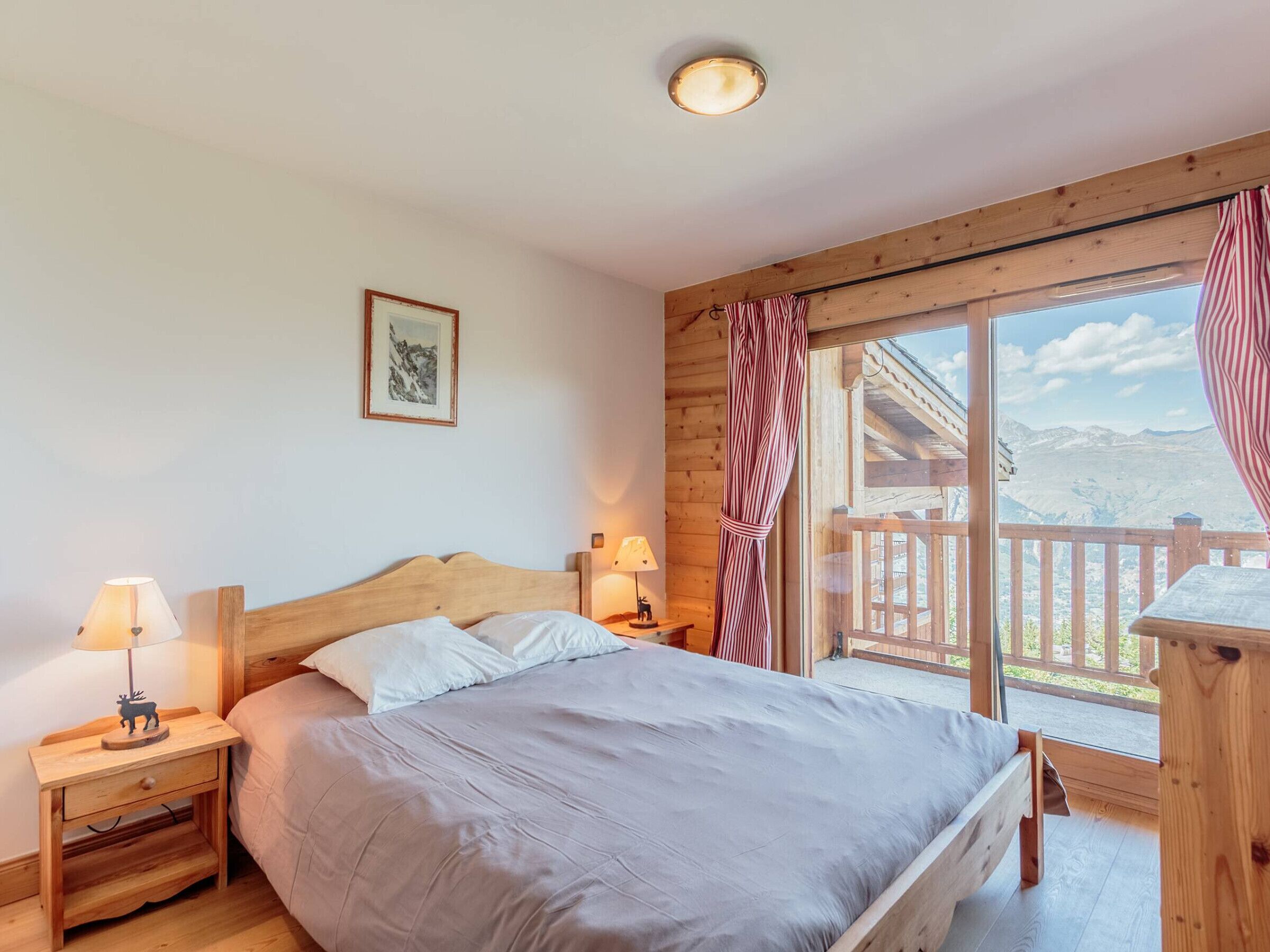 A bedroom with a wooden bed, two bedside tables with lamps, a window with curtains, and a mountain view.