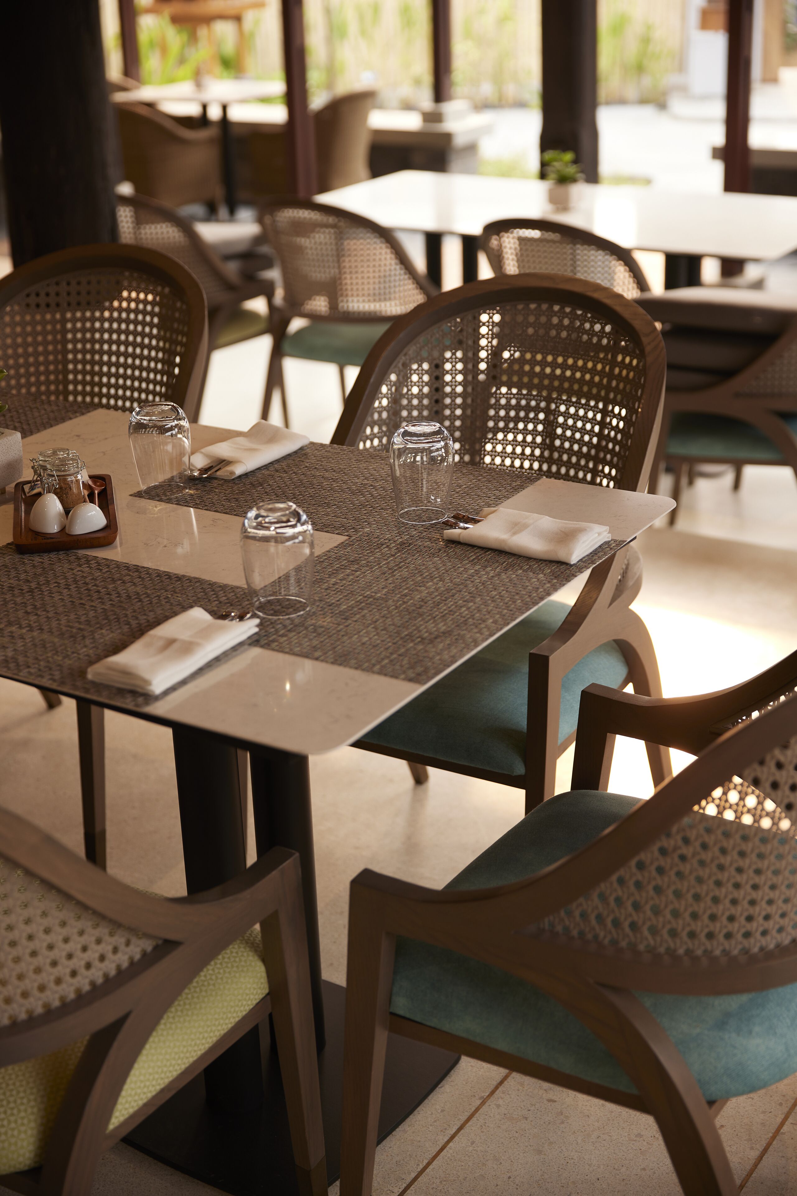 A dining area with a table set for two, featuring woven chairs and a woven table runner.