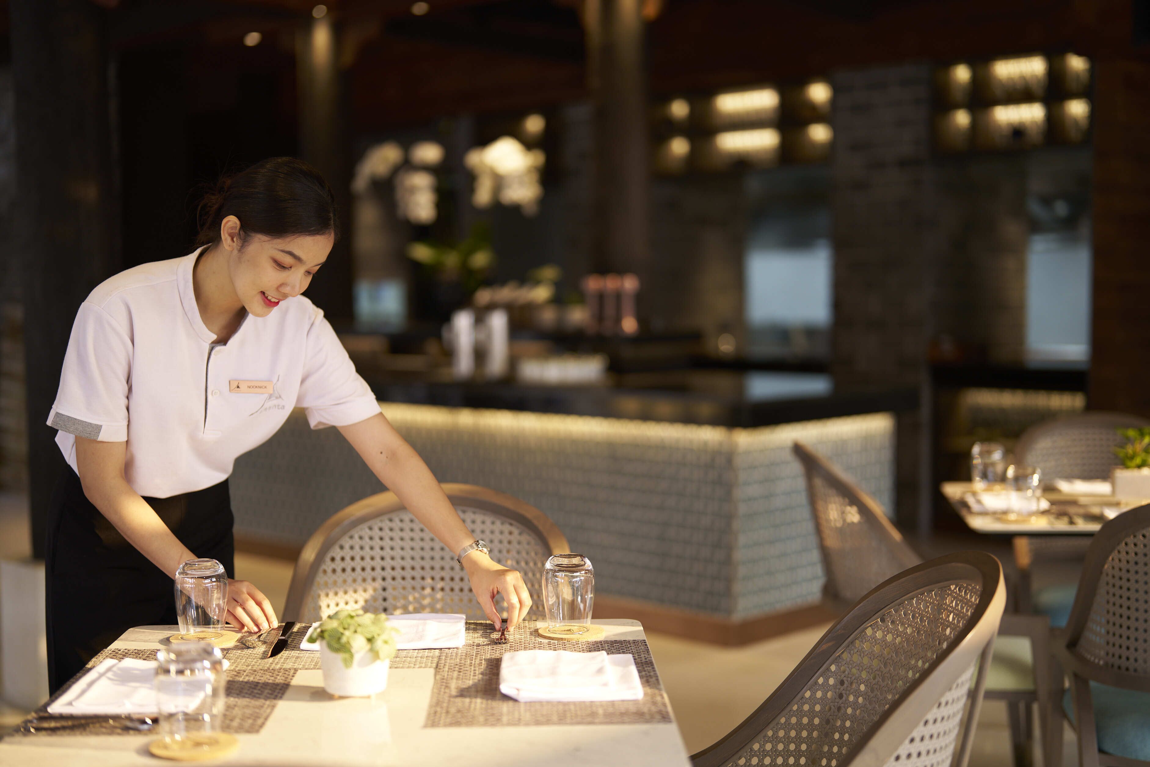 A restaurant setting with a waiter setting a table.