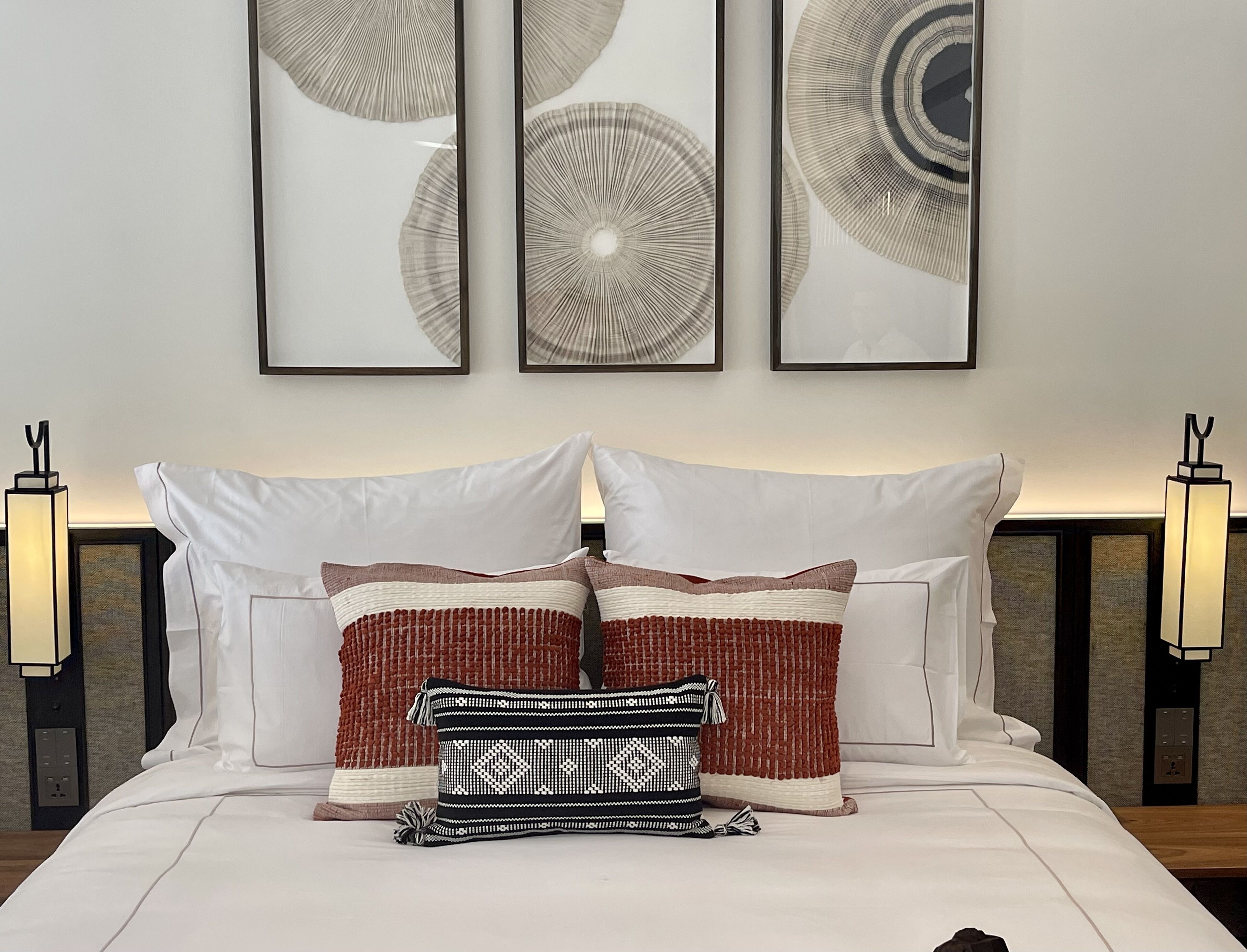 Un lit bien fait, avec du linge de lit blanc et des coussins décoratifs, des œuvres d’art encadrées au mur et des lampes de chevet.