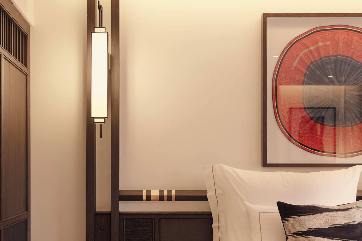 Een hotelkamer met een bed, een rode bijzettafel, een kunstwerk aan de muur en een modern lamp.