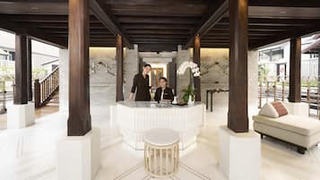 A reception area with a reception desk, two staff members, a small round table, and a sofa with a cushion.