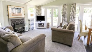 A living room with a fireplace, television, and seating area. - Orchard Lodge (Pwllheli)