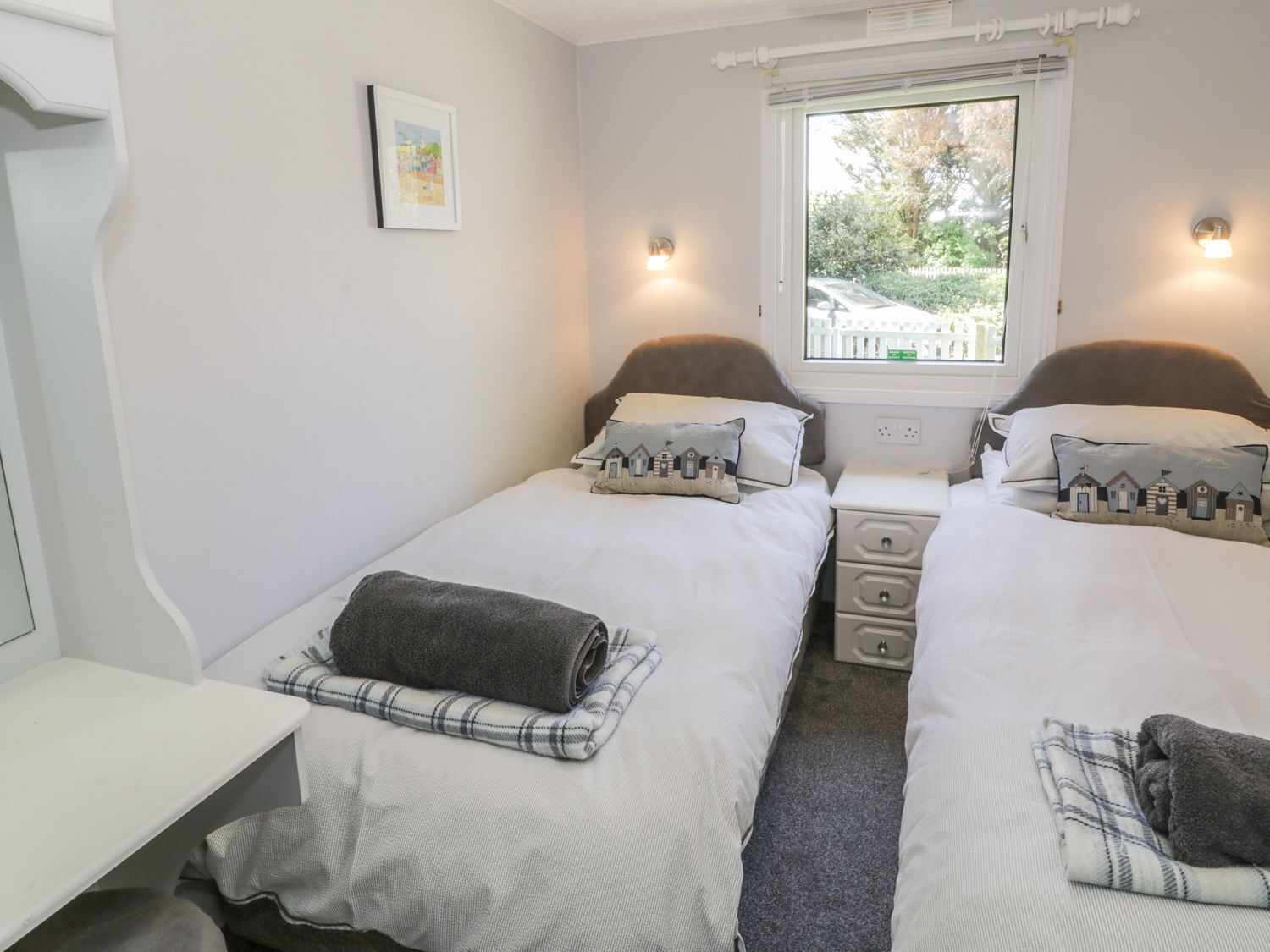 A twin room with two beds, a small table, a window with a view of the outside, and a wall-mounted picture.