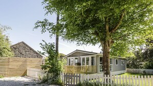 A single-story house with a gravel driveway, surrounded by a wooden fence and a tree. - Orchard Lodge (Pwllheli)