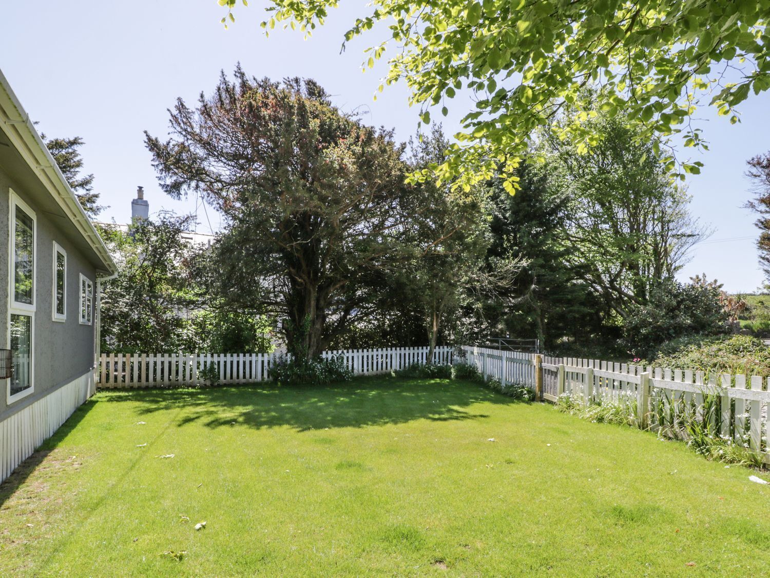 A well-maintained lawn with a white picket fence, a large tree, and a building with a chimney.