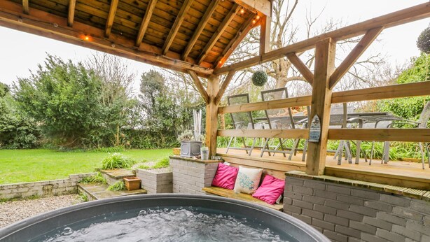 Una vasca idromassaggio sotto un gazebo in legno, con un muro in mattoni e una panca con cuscini.