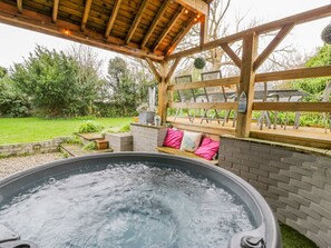 A hot tub under a wooden pergola with a brick wall and a bench with cushions. - The Orchard (Pwllheli)