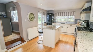 Una cucina moderna con pavimento in legno, mobili bianchi, un'isola centrale e piano cottura integrato.