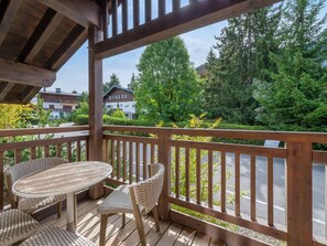 A wooden deck with a table and chairs, overlooking a road and greenery.