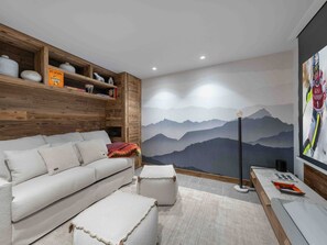 A modern living room with a sofa, ottomans, wooden shelves, and a mountain landscape mural.