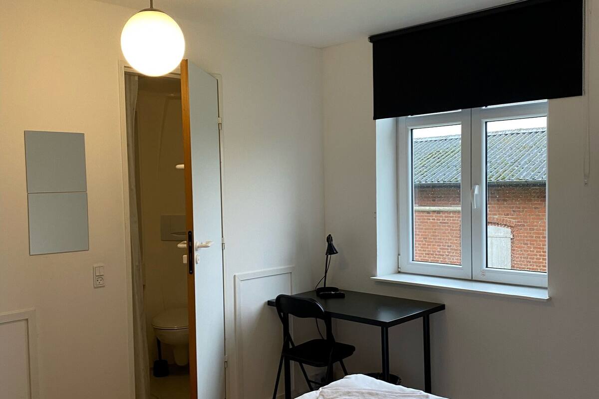 Une chambre avec deux lits, un bureau et une fenêtre donnant sur un immeuble en briques.
