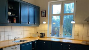 A kitchen with blue cabinets, a dishwasher, a sink, and a window with a view of trees. - Only Sleep Femern (Holeby)