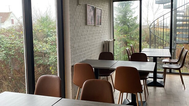 A dining area with tables and chairs, large windows, and a brick wall with framed pictures. - Only Sleep Femern (Holeby)
