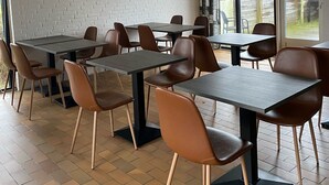 A dining area with tables and chairs, a white brick wall, and a large window with a view of trees. - Only Sleep Femern (Holeby)